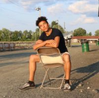 Aahnix poses for a picture on a chair, facing the sunset.