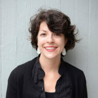 Dr. Bergelson smiles in front of a grey-painted wooden wall