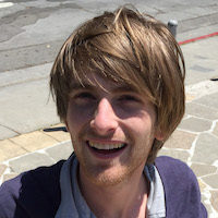 Stephan smiles while standing on a smooth stone sidewalk