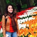 Carla stands next to a bed of red, white, orange, and yellow tulips.