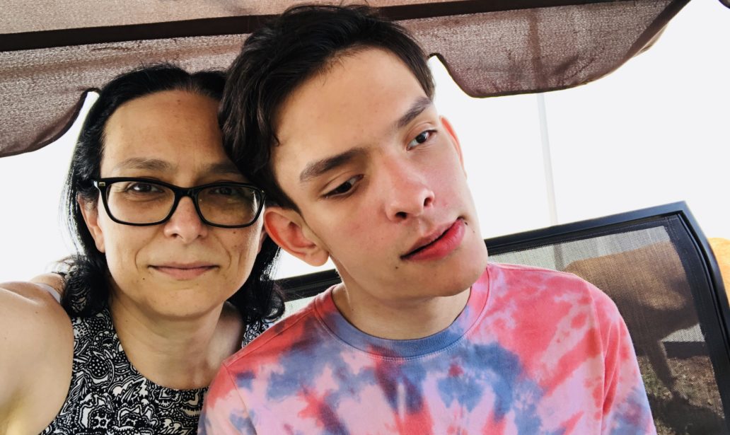 A selfie showing Amber on the left and Ivan on the right. Amber has long, dark brown hair, and wears a black and white patterend shirt and glasses. Ivan has short, dark brown hair and wears a red and blue tie-dye t-shirt.