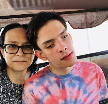 A selfie showing Amber on the left and Ivan on the right. Amber has long, dark brown hair, and wears a black and white patterend shirt and glasses. Ivan has short, dark brown hair and wears a red and blue tie-dye t-shirt.