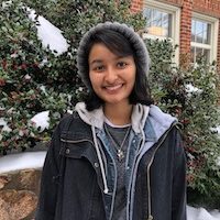 Jen stands smiling in front of a snowy background wearing a grey beanie and a navy jacket.