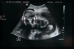 A grainy ultrasound readout with a pair of gray headphones superimposed over the fetus' head.