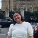 Stephanie, with a black bob and a white dress, smiles in front of Buckingham Palace.